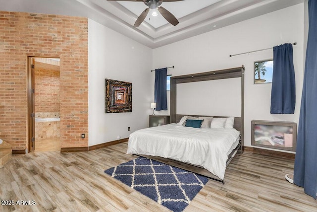bedroom with a raised ceiling, ensuite bath, baseboards, and wood finished floors