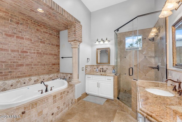 full bathroom featuring two vanities, a shower stall, a bath, ornate columns, and a sink