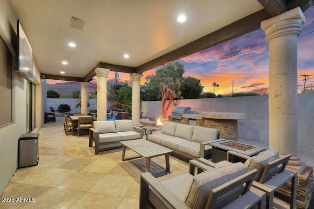 patio terrace at dusk featuring an outdoor living space with a fire pit, area for grilling, an outdoor kitchen, and outdoor dining area