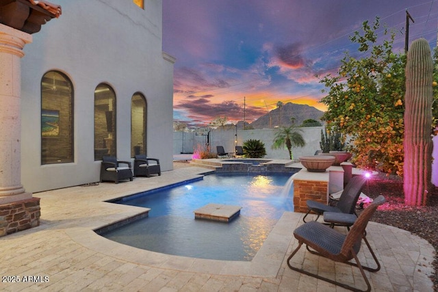 pool at dusk featuring a patio area, a pool with connected hot tub, and fence