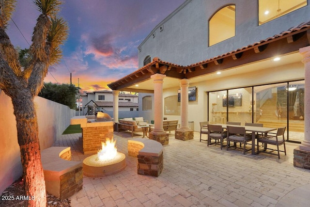 patio terrace at dusk featuring an outdoor fire pit, a fenced backyard, and outdoor dining area