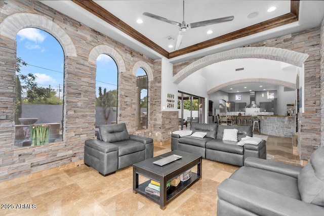 living room featuring arched walkways, a towering ceiling, a ceiling fan, and ornamental molding