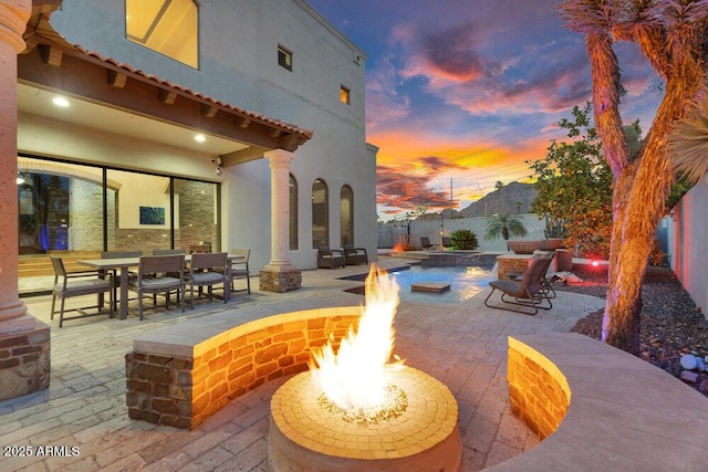 patio terrace at dusk with fence, a fire pit, and outdoor dining area