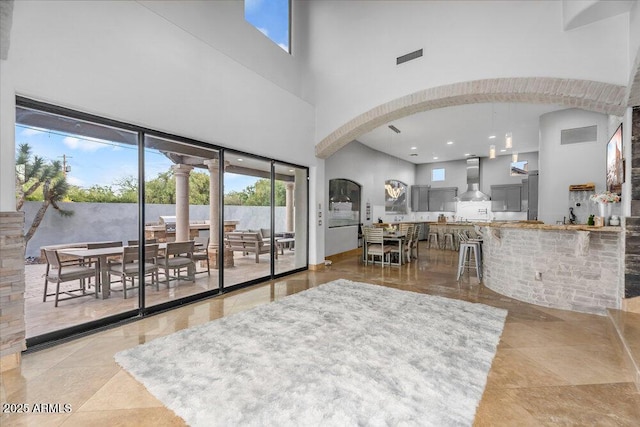 living room featuring arched walkways, visible vents, and a high ceiling