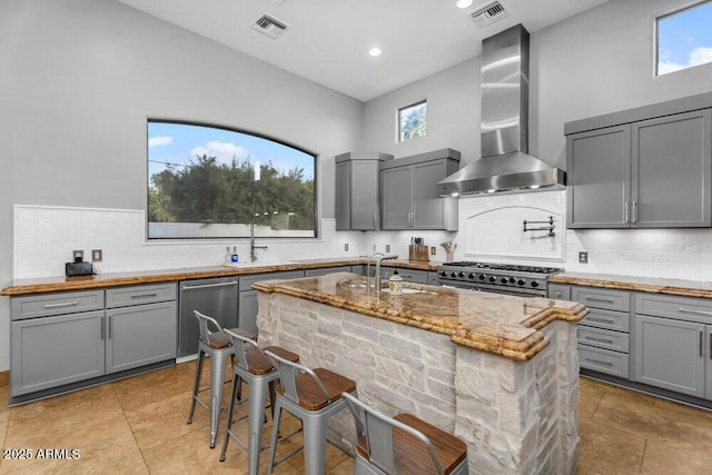 kitchen featuring gray cabinets, appliances with stainless steel finishes, wall chimney range hood, and visible vents