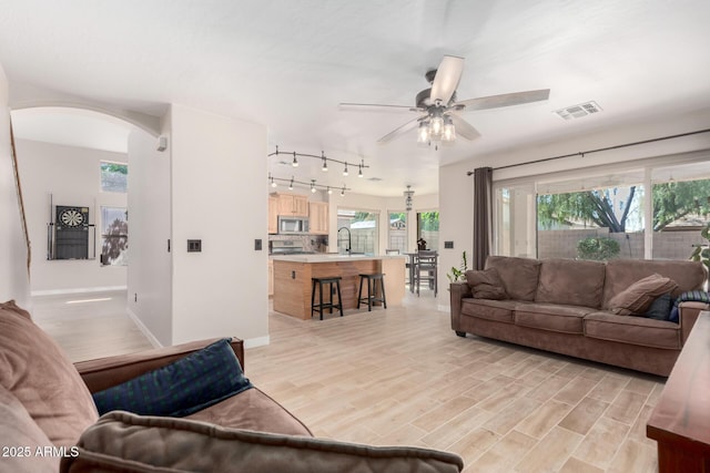 living area with arched walkways, a ceiling fan, baseboards, and light wood-style flooring