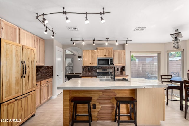 kitchen featuring stainless steel appliances, light brown cabinetry, a sink, backsplash, and a kitchen bar