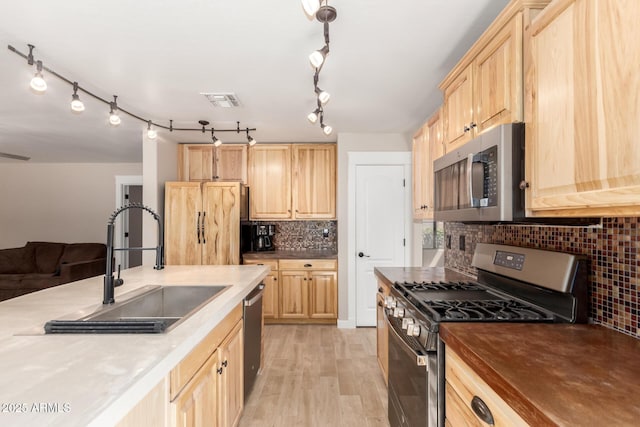 kitchen with appliances with stainless steel finishes, light brown cabinetry, backsplash, a sink, and light wood-style floors