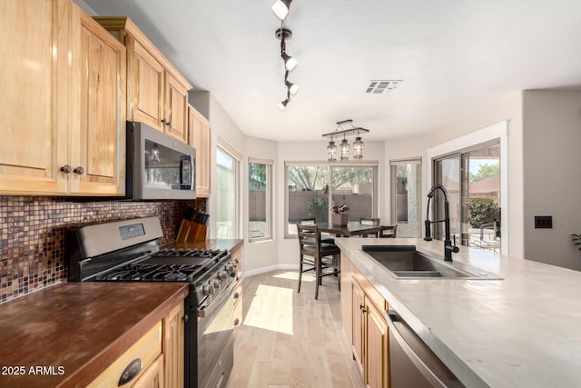 kitchen with appliances with stainless steel finishes, a sink, decorative backsplash, light wood-type flooring, and light brown cabinets