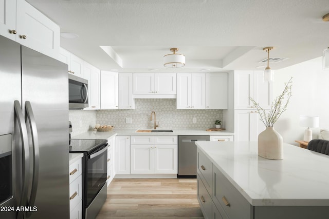 kitchen with appliances with stainless steel finishes, tasteful backsplash, a raised ceiling, light wood-type flooring, and white cabinets