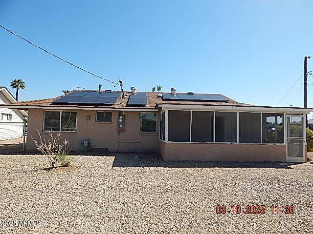 rear view of property featuring roof mounted solar panels, stucco siding, and a sunroom