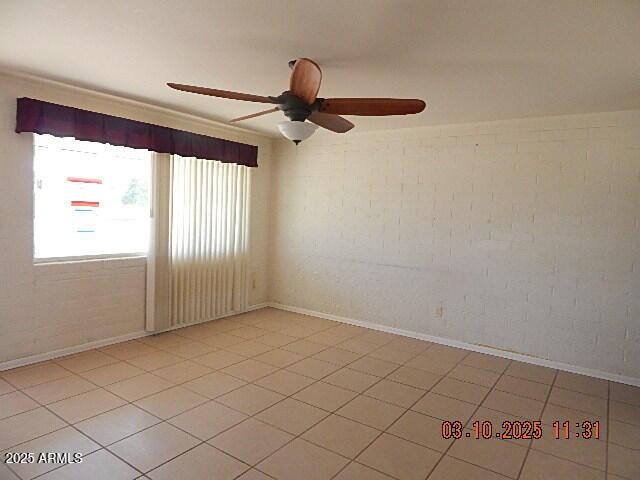 spare room featuring light tile patterned floors, ceiling fan, and brick wall