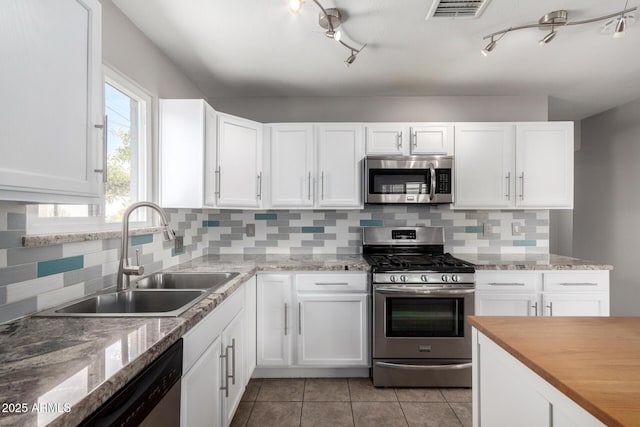 kitchen featuring appliances with stainless steel finishes, sink, white cabinets, decorative backsplash, and light tile patterned floors