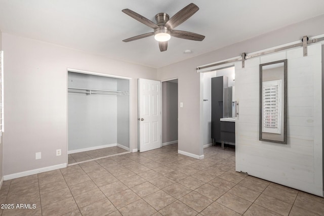 unfurnished bedroom featuring light tile patterned flooring, ceiling fan, a barn door, and a closet