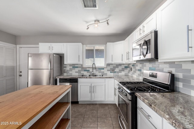 kitchen featuring sink, dark tile patterned floors, appliances with stainless steel finishes, white cabinetry, and light stone countertops