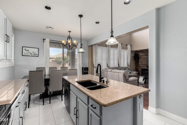 kitchen with sink, hanging light fixtures, a stone fireplace, a chandelier, and a kitchen island with sink