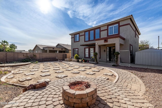 rear view of property featuring a shed, a fire pit, and a patio area