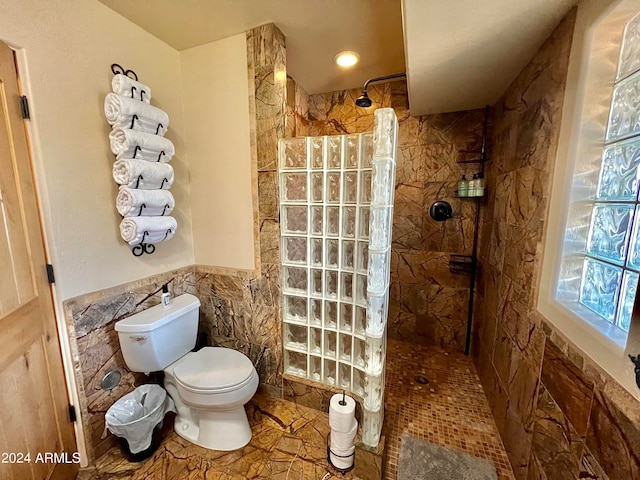 bathroom with tile walls, toilet, tiled shower, and tile flooring