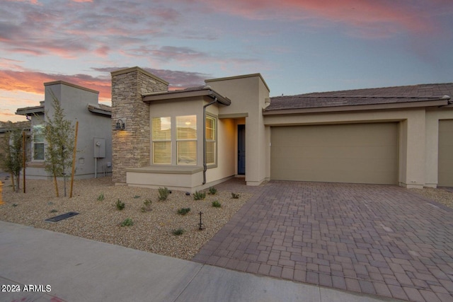 view of front of house with an attached garage, stone siding, decorative driveway, and stucco siding