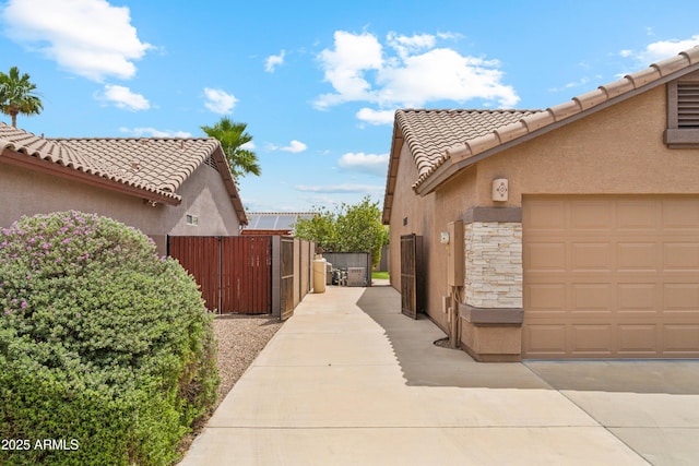 10341 E Dragoon Ave, Mesa, AZ 85208 - view of side of home featuring stucco siding, a tiled roof, stone siding, a gate, and a garage