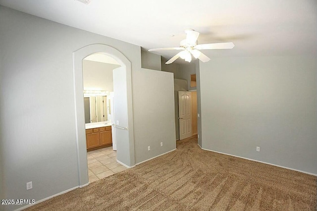 unfurnished bedroom featuring arched walkways, light colored carpet, ensuite bath, and ceiling fan