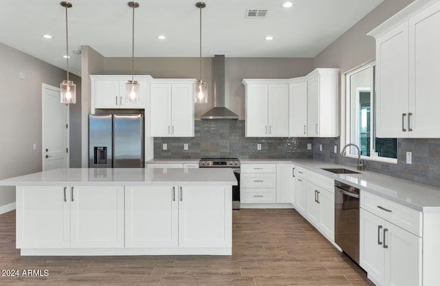 kitchen featuring a kitchen island, wall chimney range hood, stainless steel appliances, sink, and pendant lighting