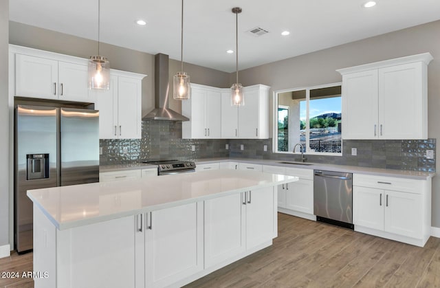 kitchen with wall chimney range hood, white cabinets, stainless steel appliances, sink, and a center island