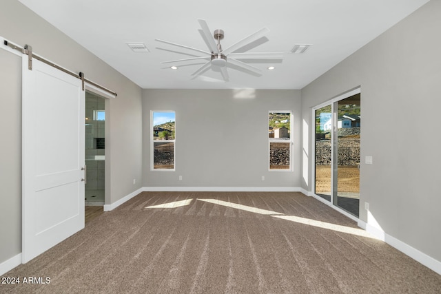 unfurnished room featuring a barn door, ceiling fan, carpet floors, and plenty of natural light