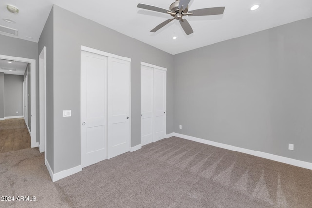 unfurnished bedroom with ceiling fan, multiple closets, and carpet flooring