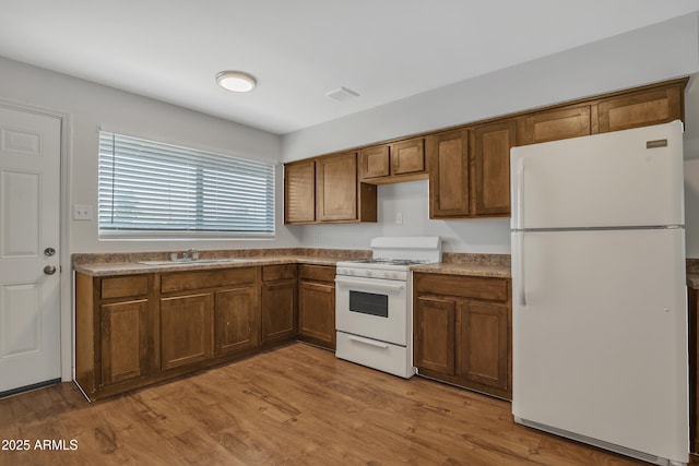 kitchen with wood finished floors, white appliances, a sink, and visible vents