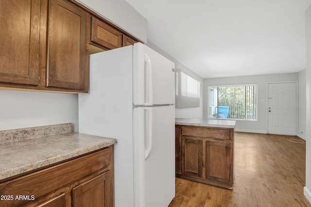 kitchen with light countertops, freestanding refrigerator, brown cabinets, and light wood finished floors