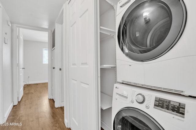 clothes washing area featuring stacked washer and dryer, laundry area, baseboards, and wood finished floors