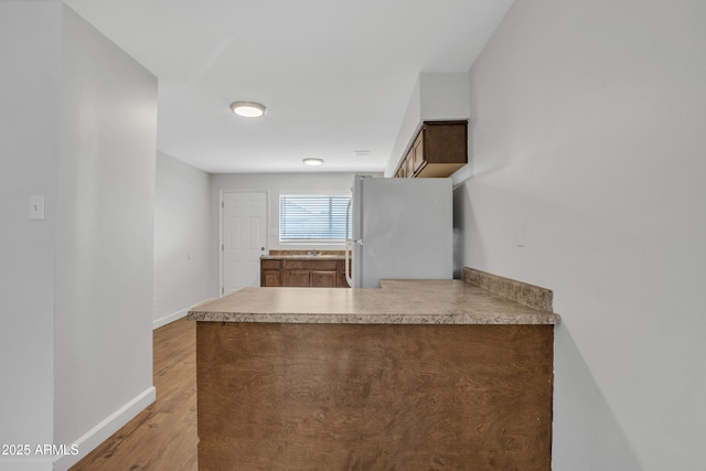 kitchen featuring a peninsula, light wood finished floors, baseboards, and freestanding refrigerator