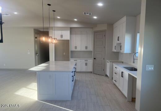 kitchen featuring recessed lighting, visible vents, white cabinetry, a kitchen island, and a sink