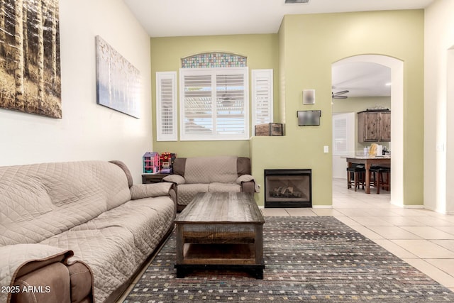 tiled living area with visible vents, a fireplace with flush hearth, baseboards, arched walkways, and a ceiling fan