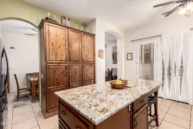kitchen with arched walkways, a ceiling fan, light stone countertops, and light tile patterned flooring