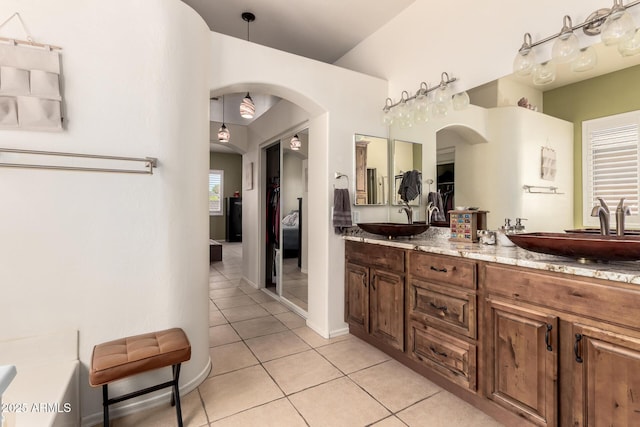 full bath with double vanity, a sink, tile patterned floors, and vaulted ceiling