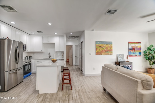 kitchen with light wood-type flooring, white cabinetry, stainless steel appliances, decorative backsplash, and a breakfast bar