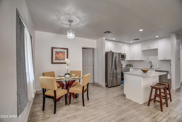 kitchen with sink, decorative light fixtures, white cabinetry, appliances with stainless steel finishes, and light hardwood / wood-style floors