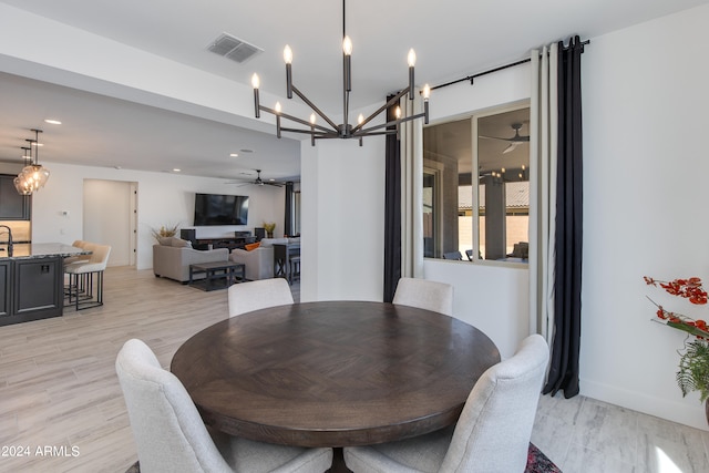 dining space with ceiling fan with notable chandelier and light wood-type flooring