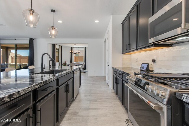 kitchen featuring dark stone counters, stainless steel appliances, hanging light fixtures, and sink