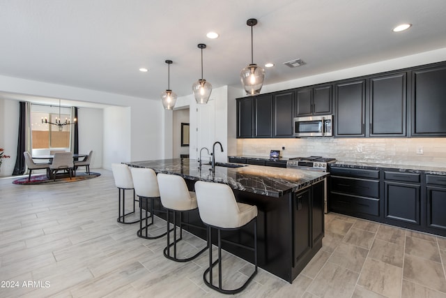 kitchen featuring an island with sink, hanging light fixtures, sink, stainless steel appliances, and a breakfast bar