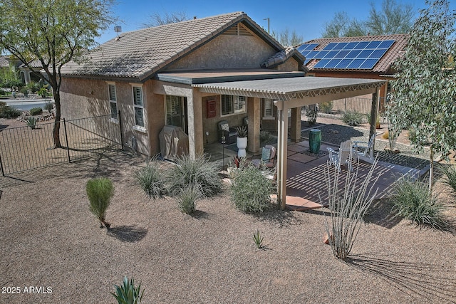 rear view of property with a patio, solar panels, fence, a tiled roof, and stucco siding