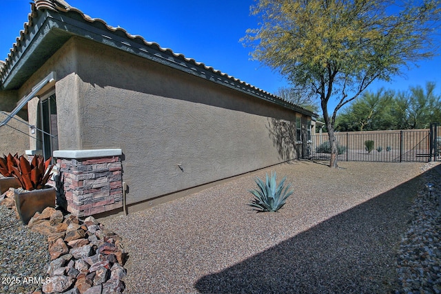 view of side of property with a tile roof, fence, and stucco siding