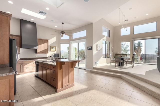 kitchen with sink, a skylight, a kitchen breakfast bar, a kitchen island with sink, and wall chimney range hood