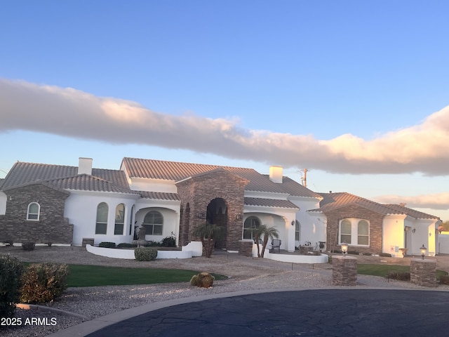 mediterranean / spanish house featuring stucco siding, stone siding, a chimney, and a tiled roof