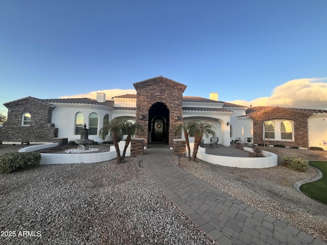 view of front of property with stucco siding, driveway, a tile roof, stone siding, and a patio area