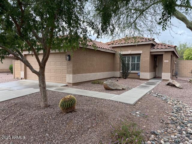 exterior space featuring an attached garage, stucco siding, a tile roof, fence, and driveway