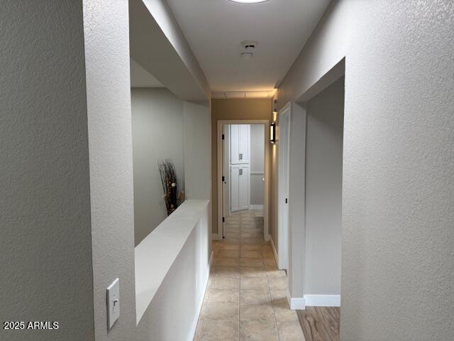 hall featuring a textured wall and light tile patterned floors