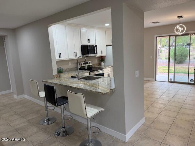 kitchen with stainless steel appliances, a breakfast bar, white cabinets, light stone countertops, and baseboards